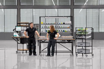 Eine Werkerin und ein Werker im Gespräch an Arbeitsplatzsystemen in einer großen Halle